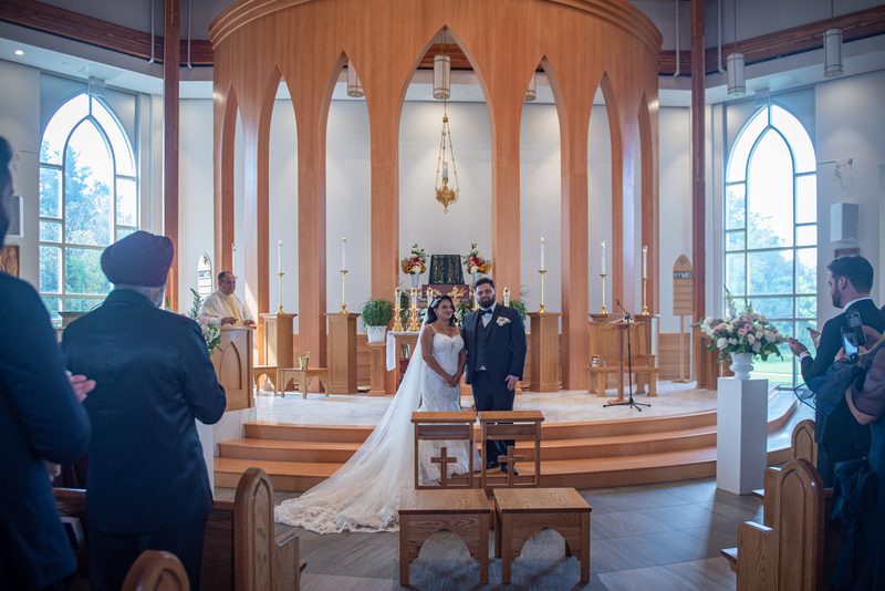 A bride and groom smile at each other during their wedding ceremony in a modern church, illuminated by natural light.