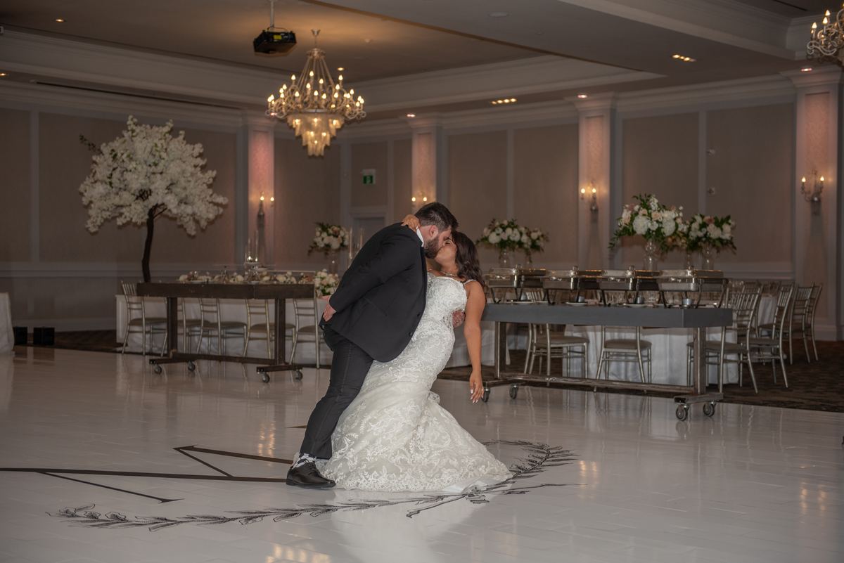 A bride and groom dance passionately in an elegantly lit ballroom, the groom dipping the bride as they kiss.