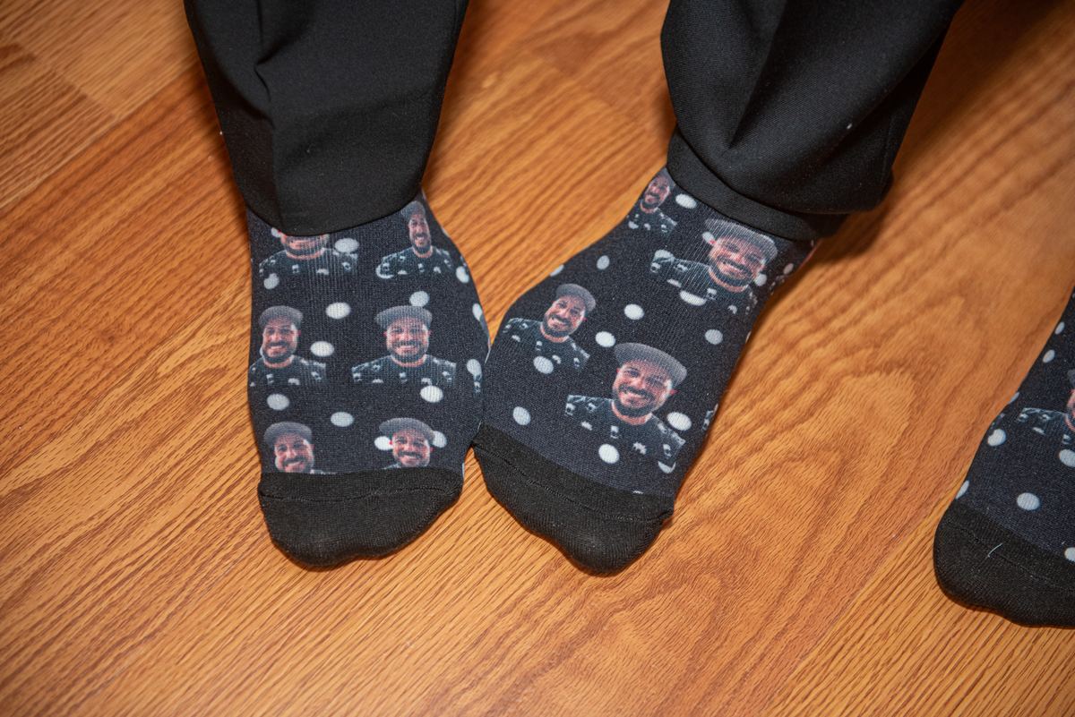 Feet in socks featuring repeated images of a smiling Black man in uniform rest on a warm wooden floor.