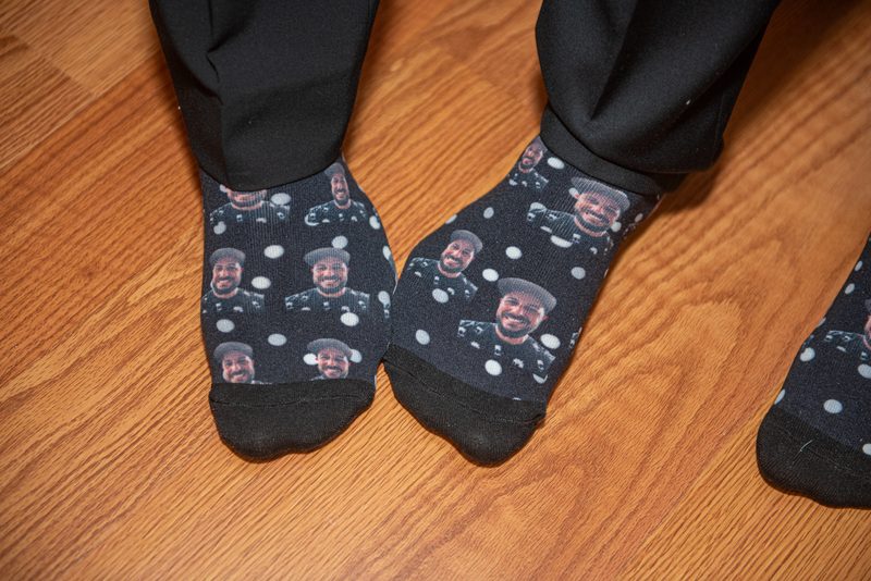 Feet in socks featuring repeated images of a smiling Black man in uniform rest on a warm wooden floor.