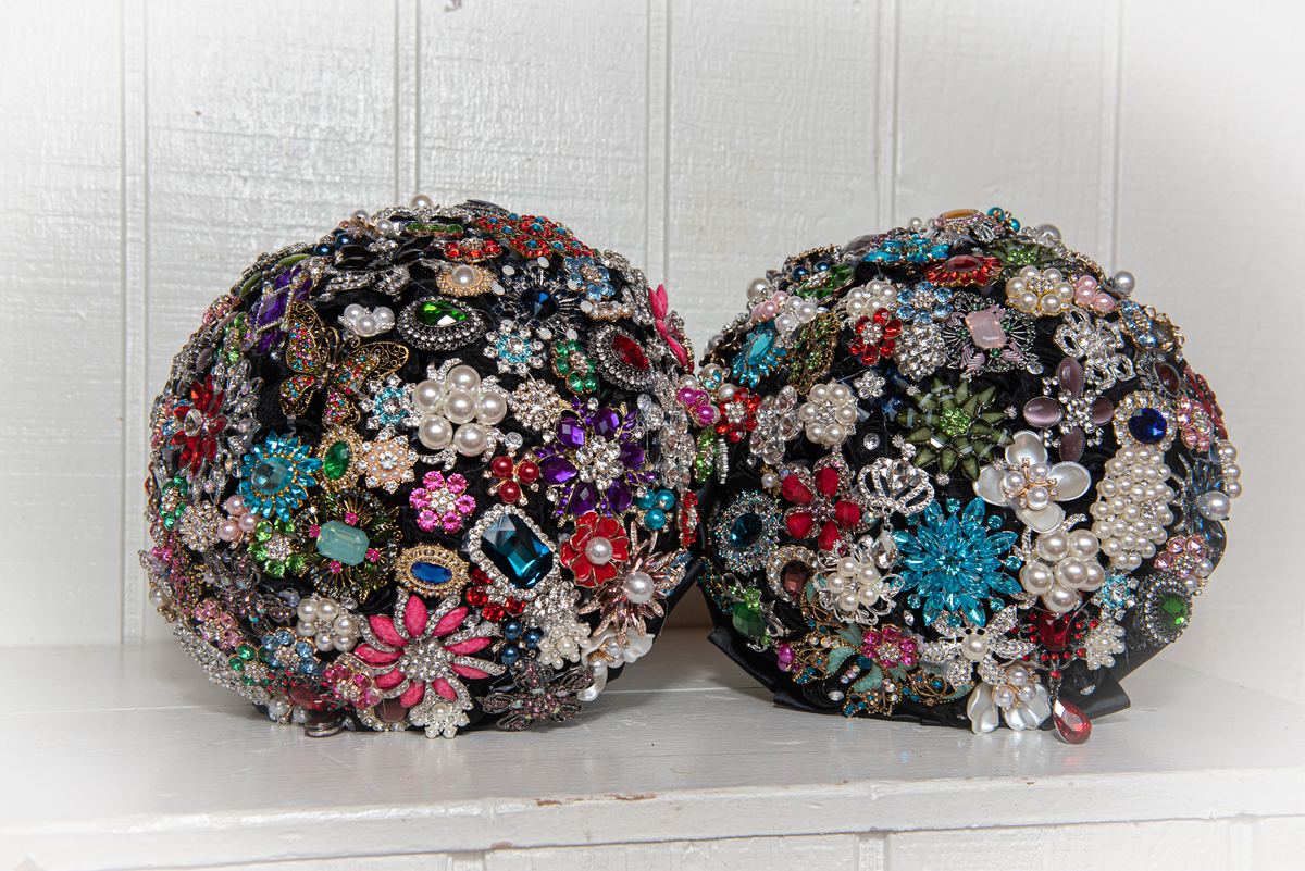 Two spherical bouquets of vintage brooches and jewels on a white surface, illuminated by soft light.