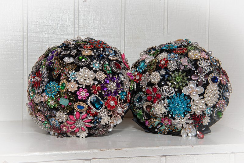 Two spherical bouquets of vintage brooches and jewels on a white surface, illuminated by soft light.