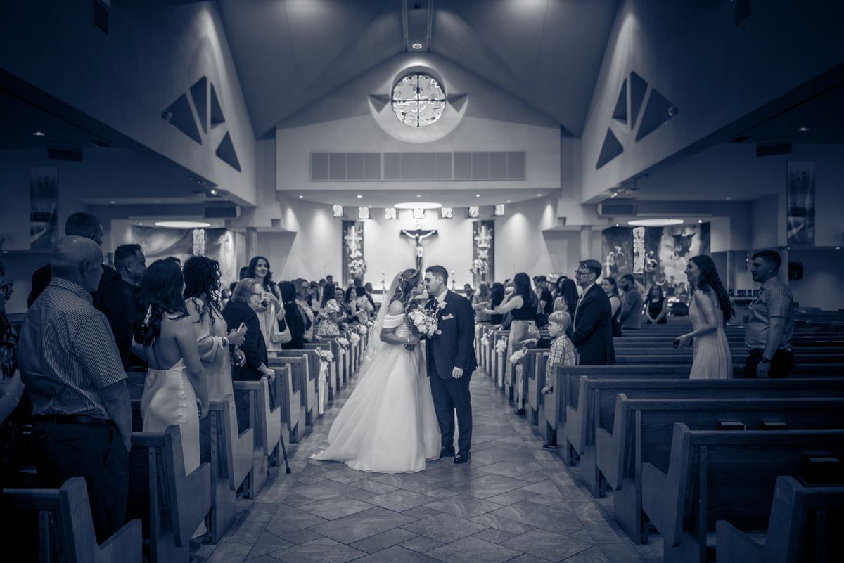 Bride and groom exchange vows at an altar, guests watching in the background of a modern church with cool lighting.