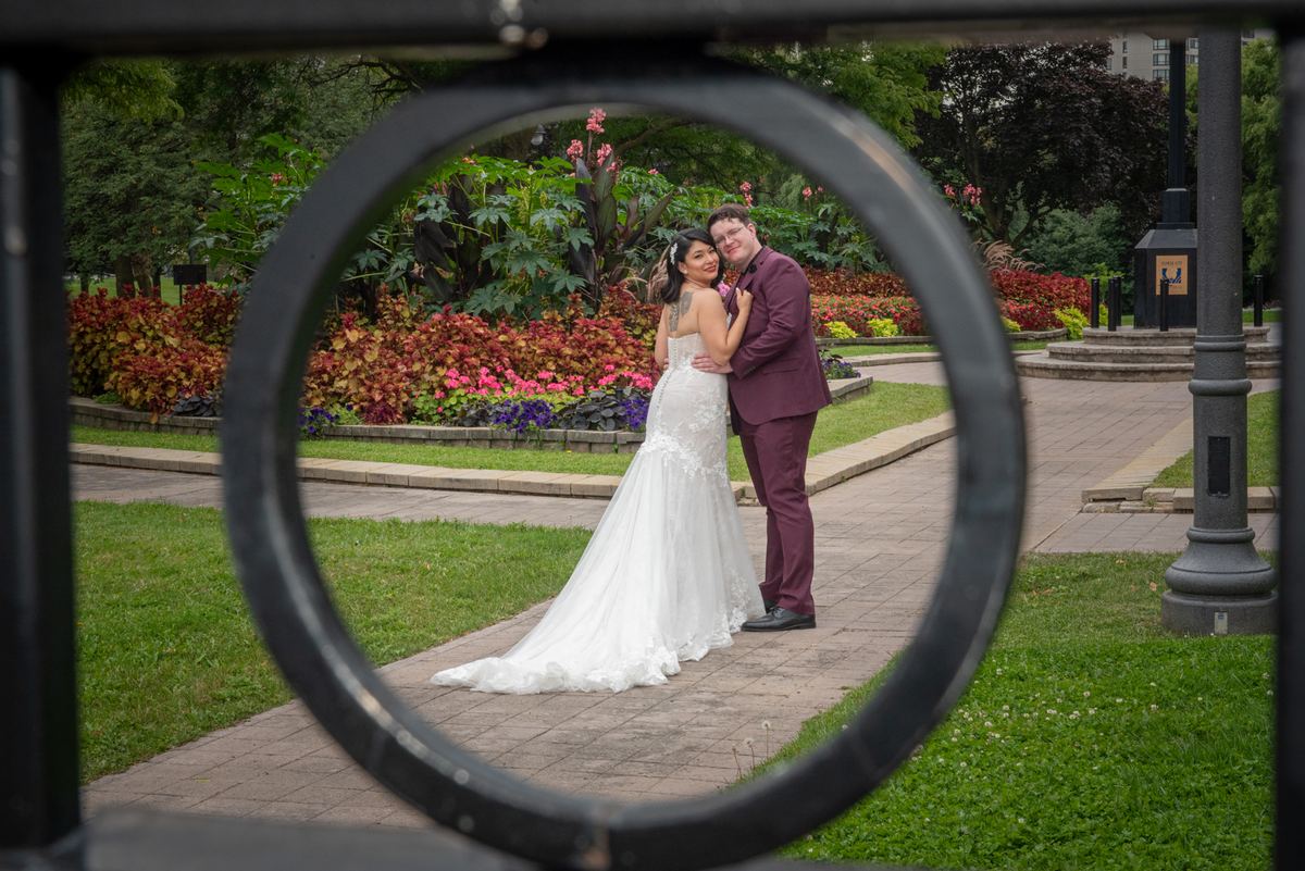 A newlywed couple embraces on a garden path surrounded by lush greenery and autumn foliage, bathed in soft daylight.