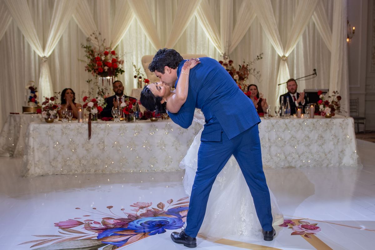A bride and groom kiss joyfully on the dance floor surrounded by guests at an elegantly decorated table.