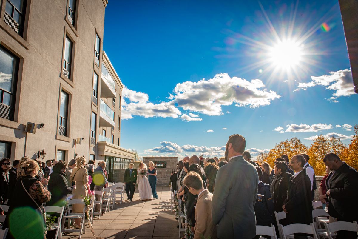 A bride and groom walk down the aisle toward an altar under a sunburst, with guests watching formally dressed on either side.
