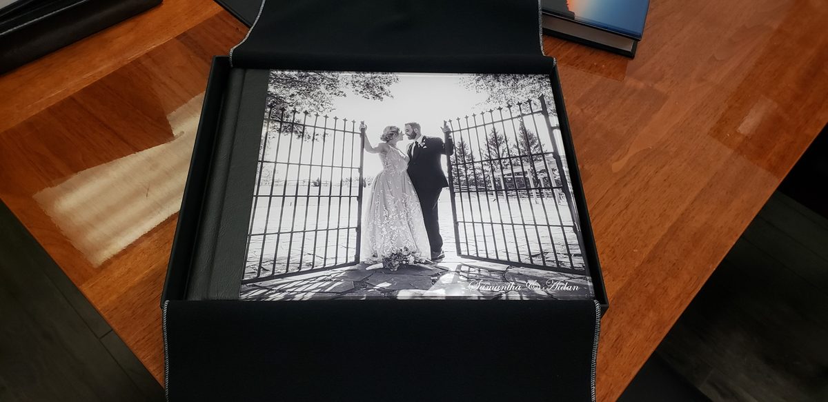A wedding album with a black-and-white acrylic cover and bonded leather spine, sitting in its black presentation box with the velvet wrap opened around it