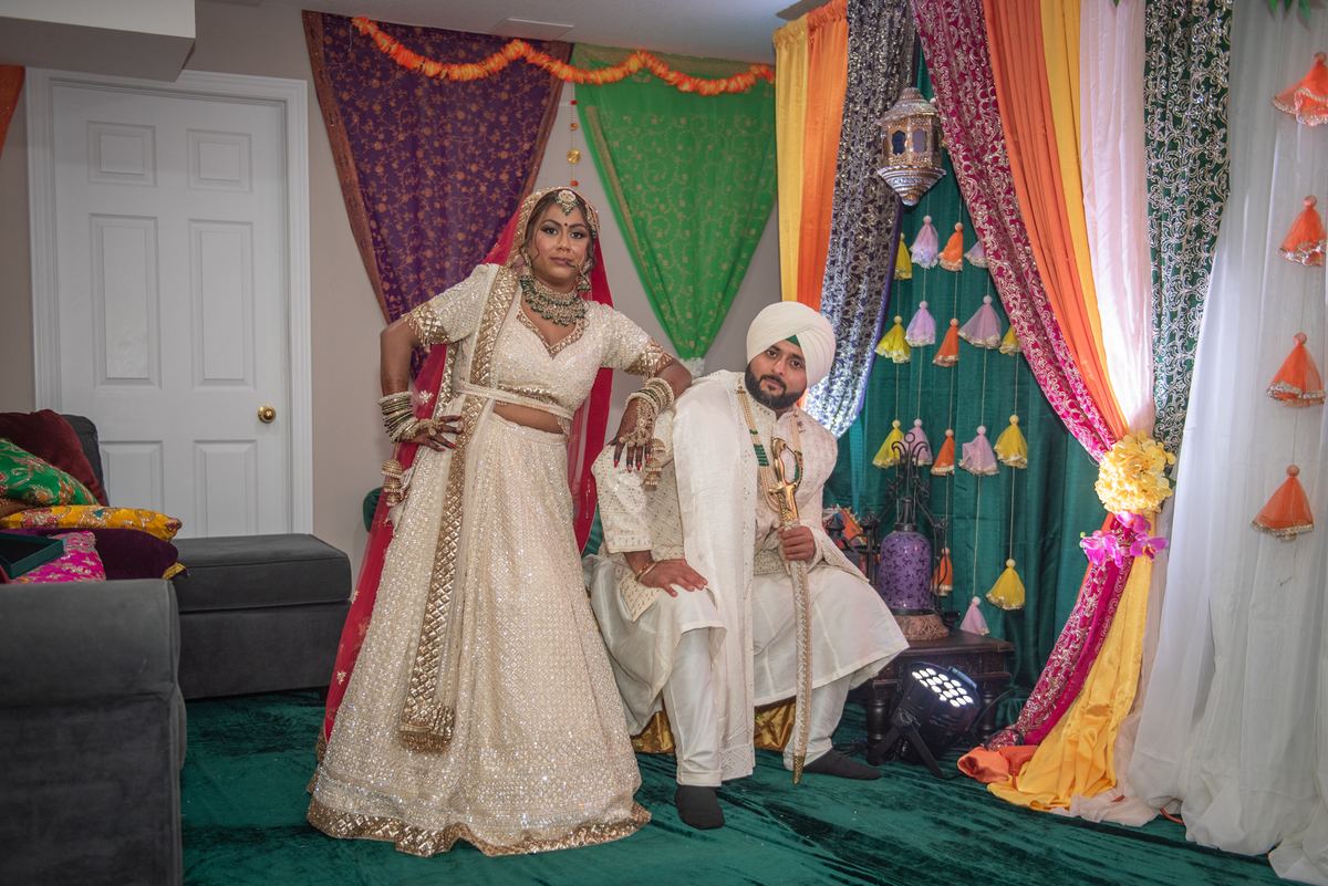 A bride and groom pose in an ornate indoor setting with colorful drapes and tassels during a pre-wedding celebration.