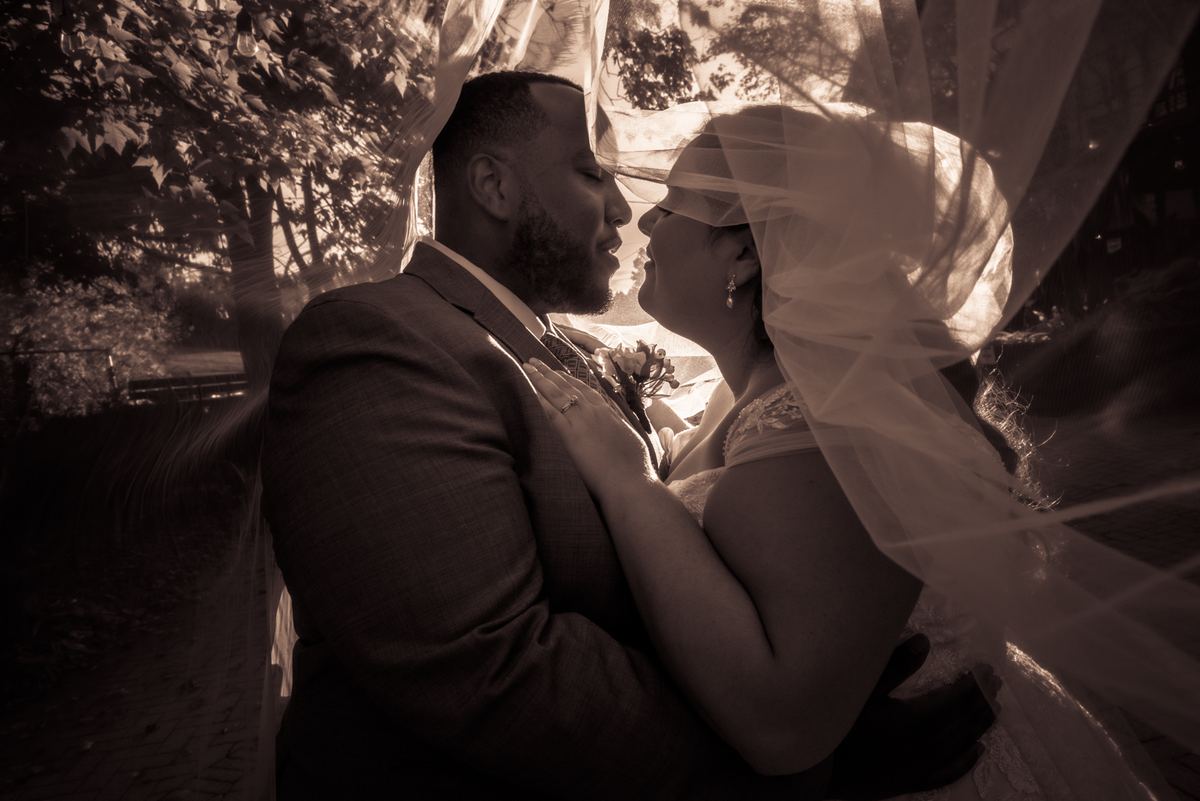 Amanda and Kyle share an intimate embrace in a sepia-toned photograph, their faces close as they gaze at each other.