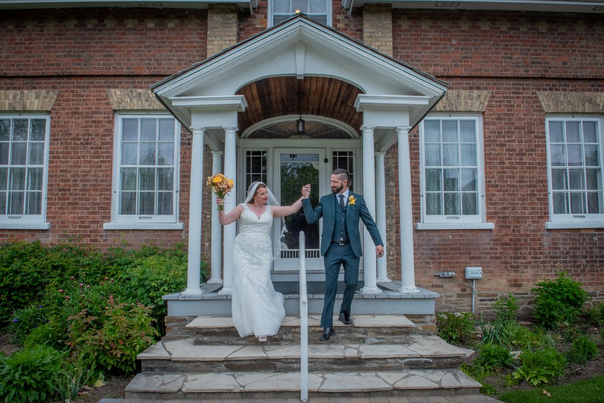 A bride and groom descend stone steps, holding hands and smiling joyfully during their wedding celebration.