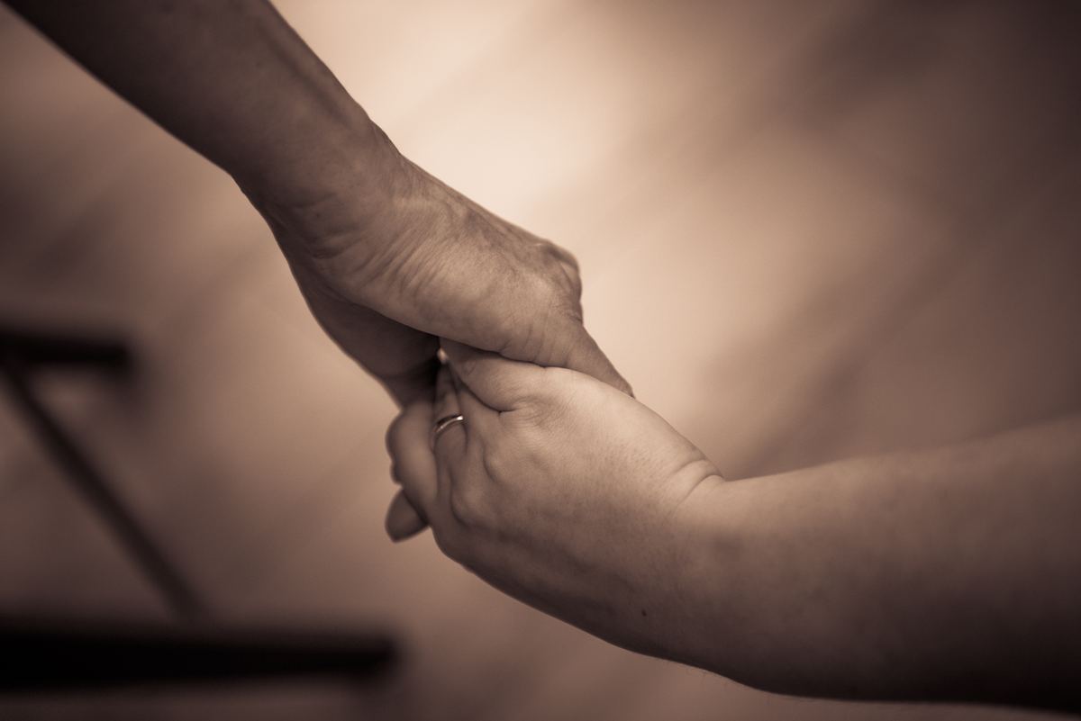 Two hands of different ages clasped together in a warm, tender embrace against a blurred background.