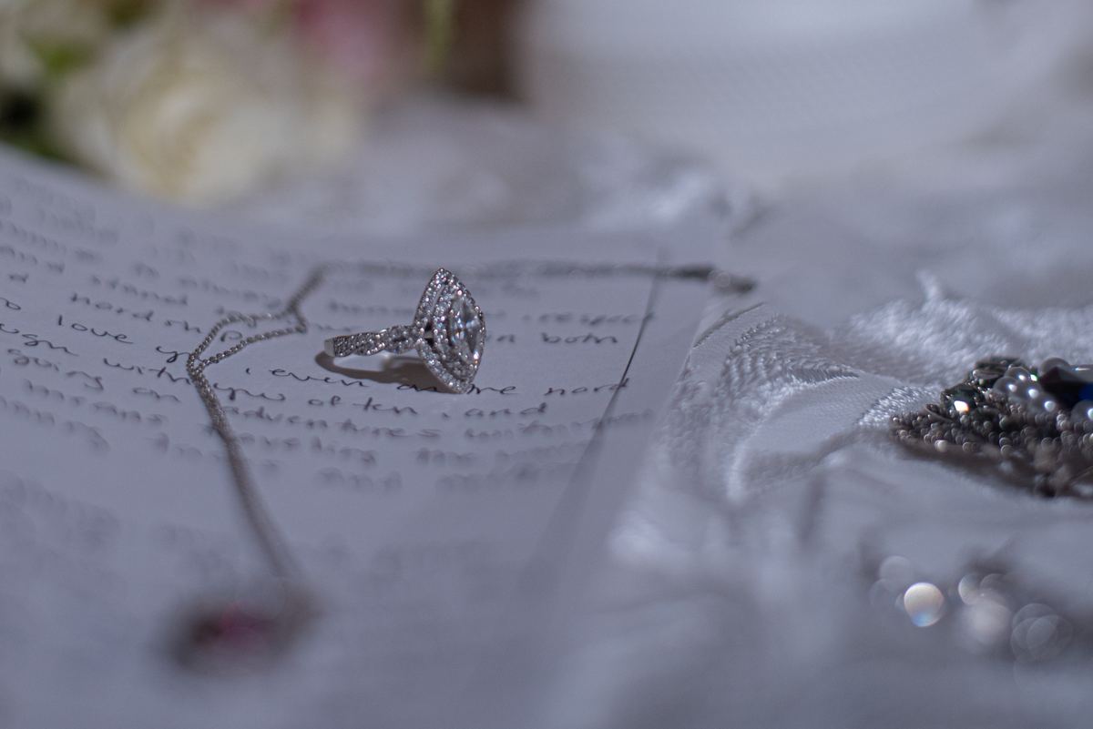 A diamond engagement ring rests on a handwritten letter surrounded by bridal accessories in soft light, symbolizing love.