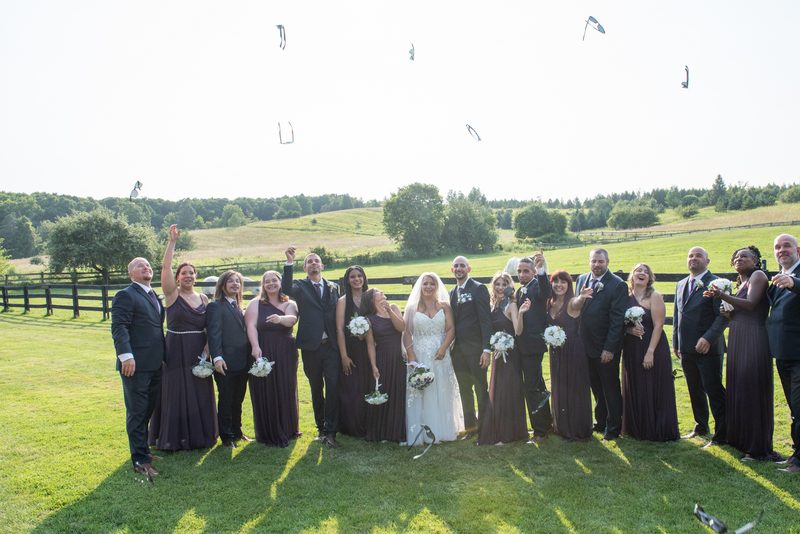 A wedding party releases white petals into the air under golden late afternoon sunlight, casting long shadows.