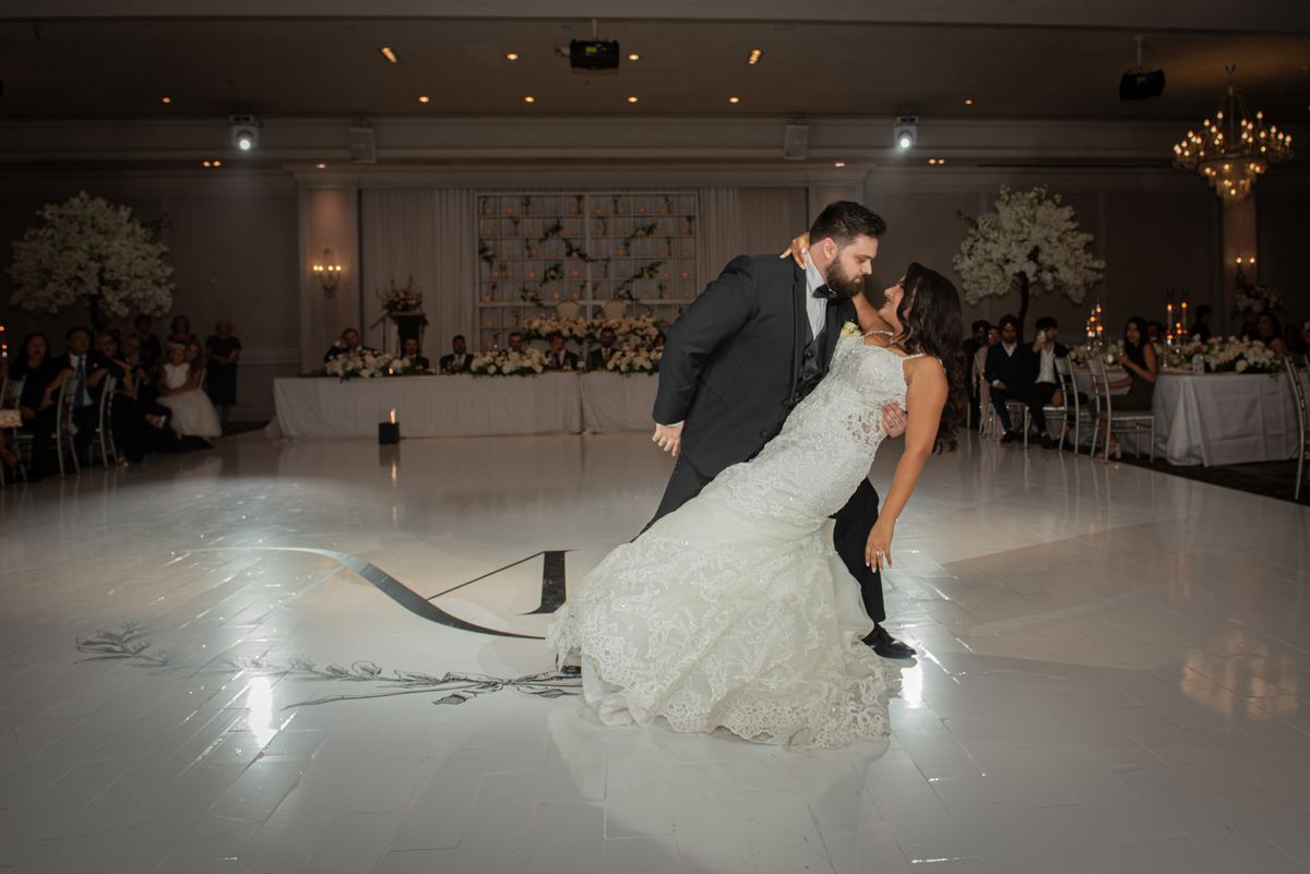 A bride and groom dance intimately in a grand ballroom, the groom dipping the bride as they gaze at each other.