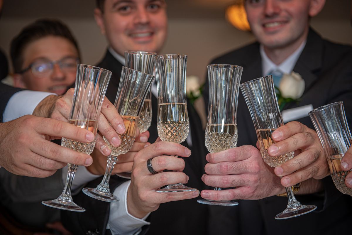 Men in suits clinking champagne glasses together at a celebration, illuminated by warm lights and smiling.