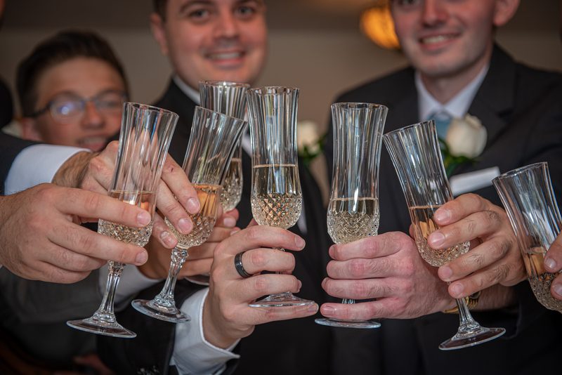 Men in suits clinking champagne glasses together at a celebration, illuminated by warm lights and smiling.