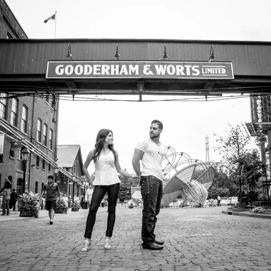 A couple walk a cobbled street beneath the Gooderham & Worts sign in Toronto's Distillery District, in black and white.