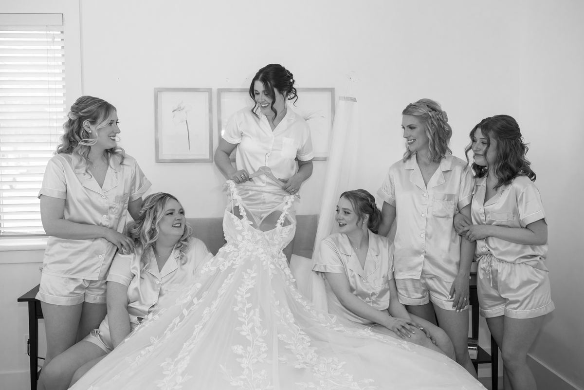 Amanda is surrounded by her bridesmaids in matching satin pajamas as she prepares to put on her wedding gown.