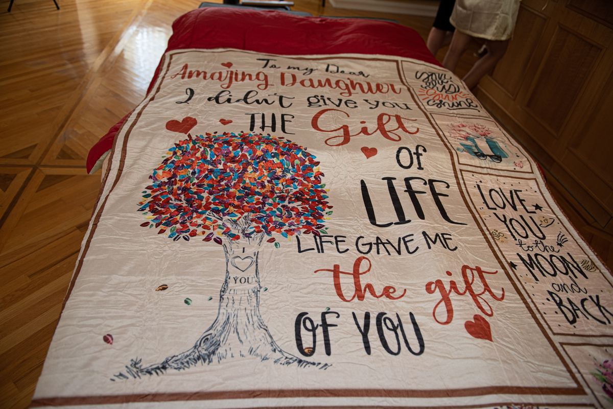 A handcrafted quilt with a message of love and a colorful tree decorates a bed in a warm, wooden-floored room.