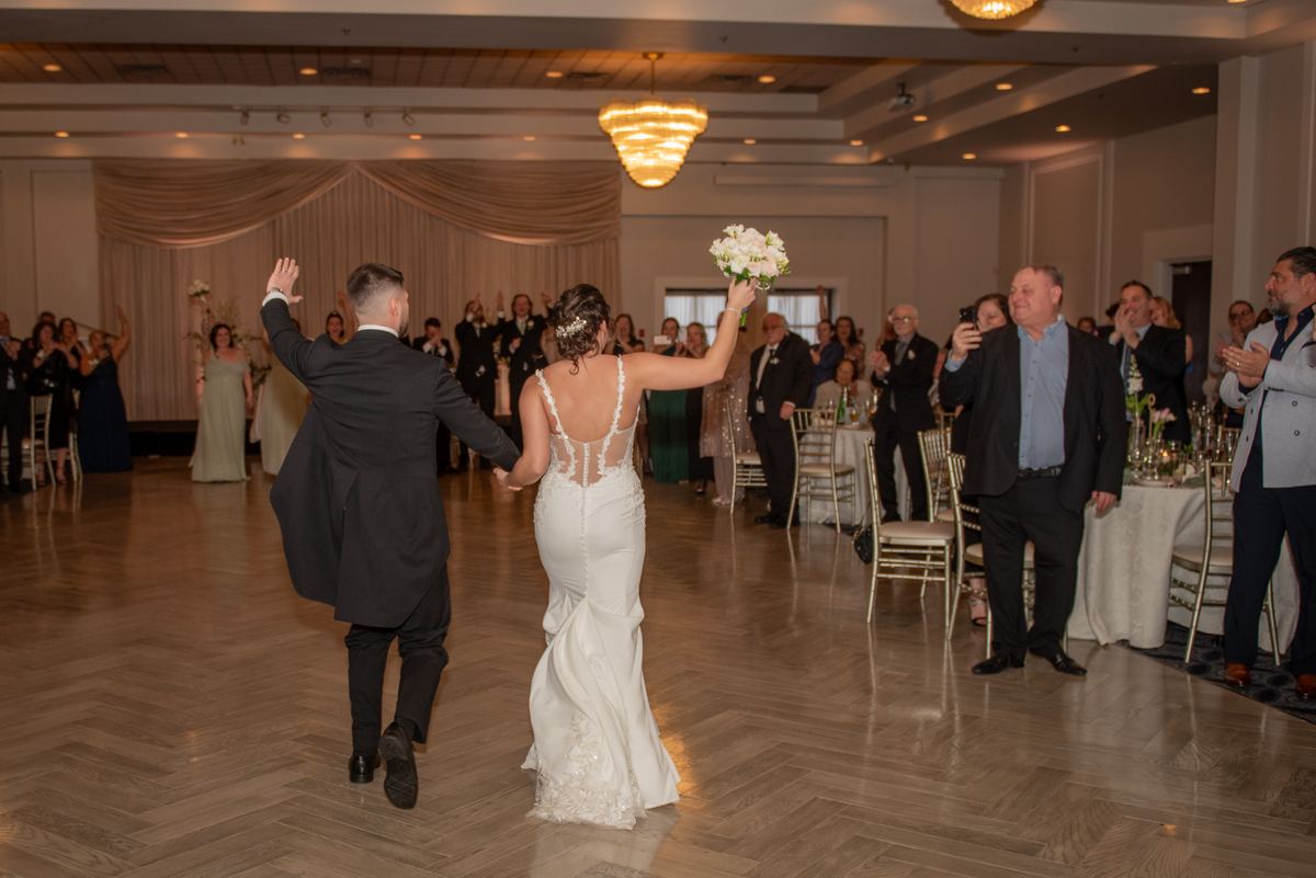 A bride and groom dance joyfully across a ballroom floor, guests cheering as they twirl with emotion.