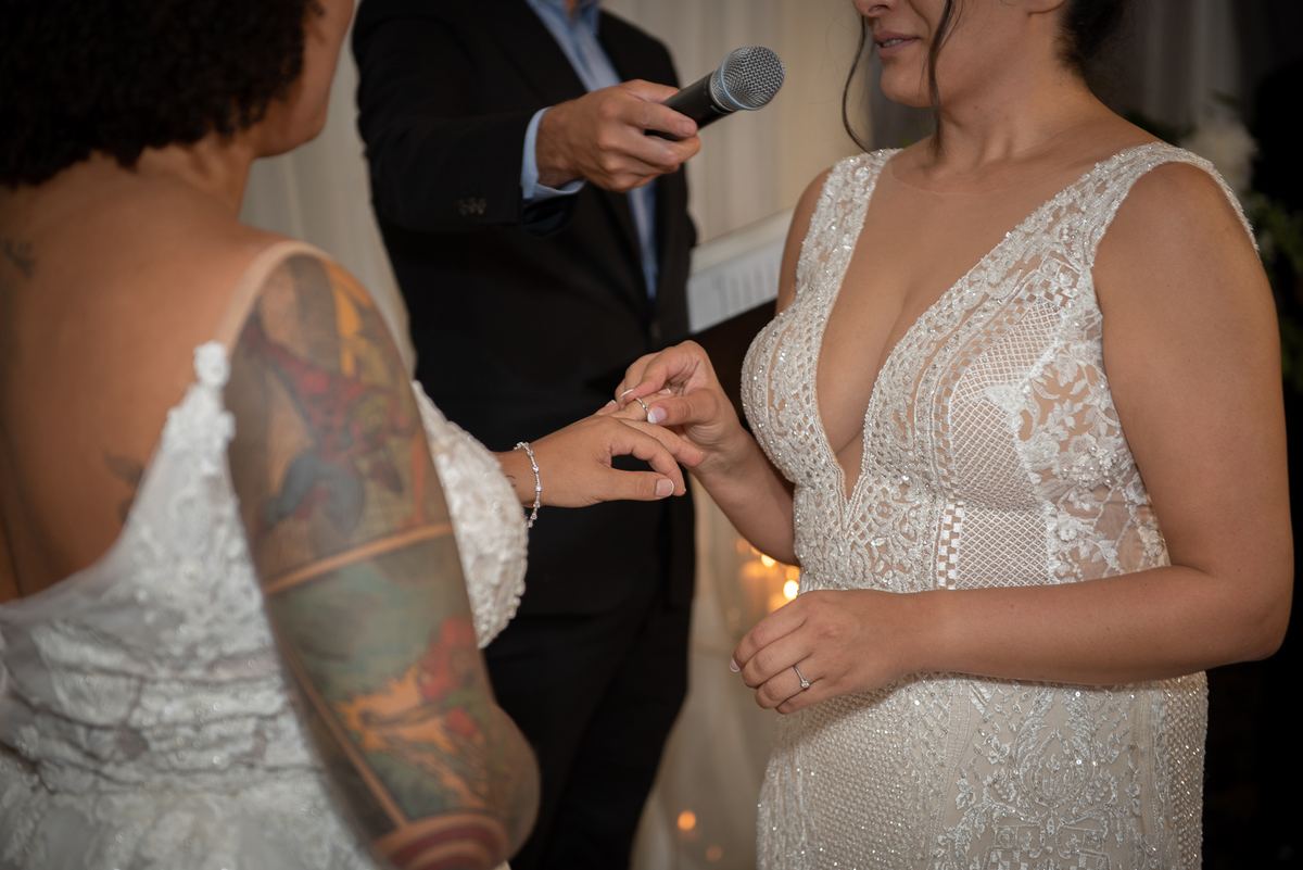 One bride places a ring on her partner's finger during an intimate ceremony with soft lighting and a celebrant.