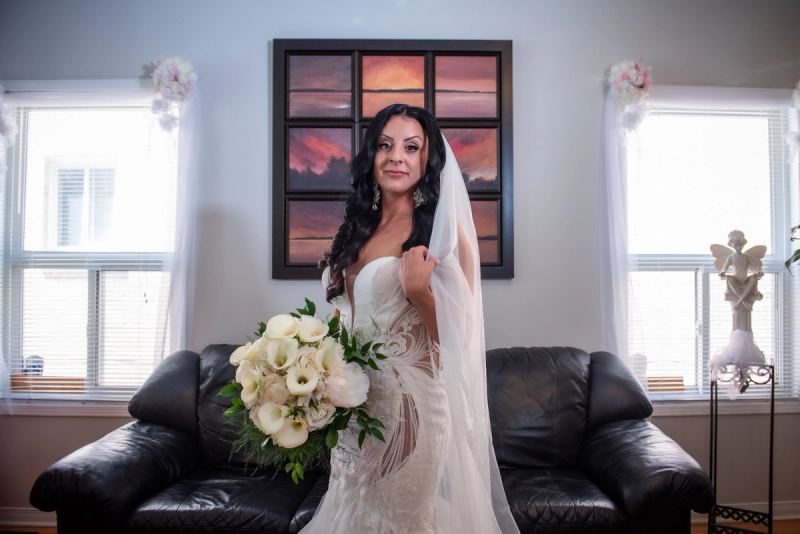 A bride in an elegant lace gown holds white calla lilies and roses, her veil draped over one shoulder.