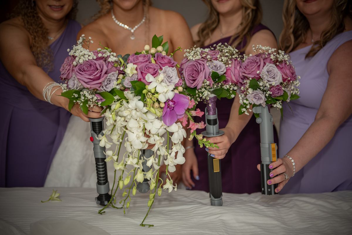 Bridesmaids hold lightsaber-shaped bouquets with white orchids and purple roses at a Star Wars-themed wedding.