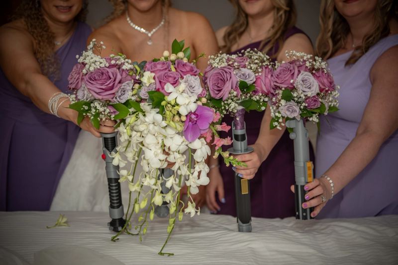 Bridesmaids hold lightsaber-shaped bouquets with white orchids and purple roses at a Star Wars-themed wedding.