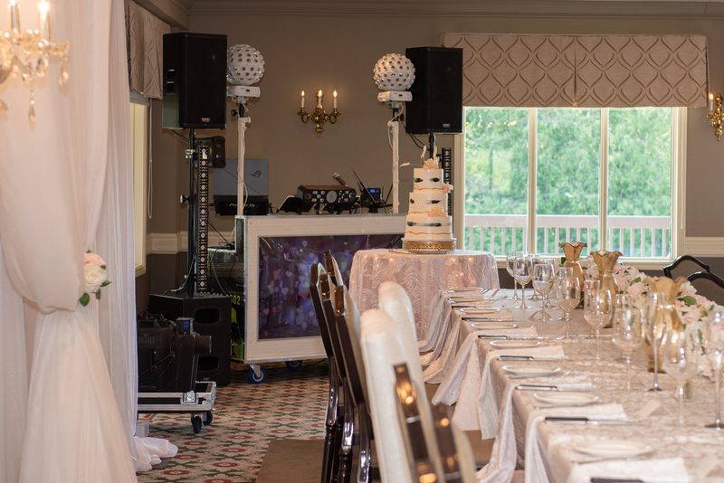 A wedding reception setup with a multi-tiered cake and banquet tables set with glassware and linens.