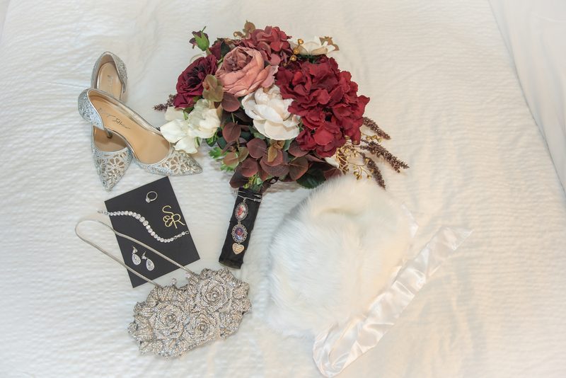 A bridal shoe, bouquet, fur stole, and jewelry set are arranged on a white surface, creating an elegant scene.