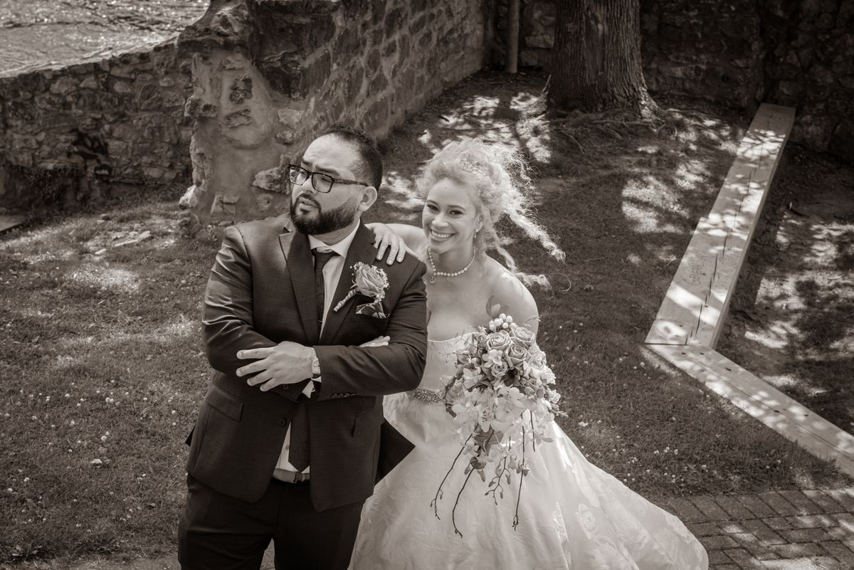 A bride and groom stand in an ancient courtyard, the bride smiling as she leans on her thoughtful partner.