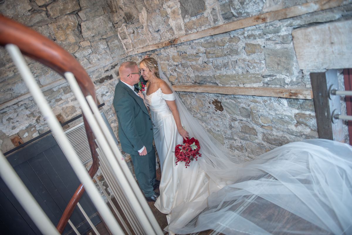A bride and groom exchange whispers on a stone staircase, illuminated by soft light and surrounded by rustic walls.