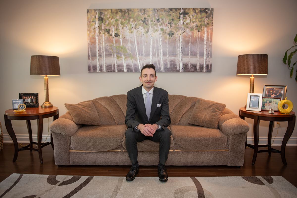 A man in a suit smiles at the camera in a living room decorated with symmetrical side tables and a birch tree painting.