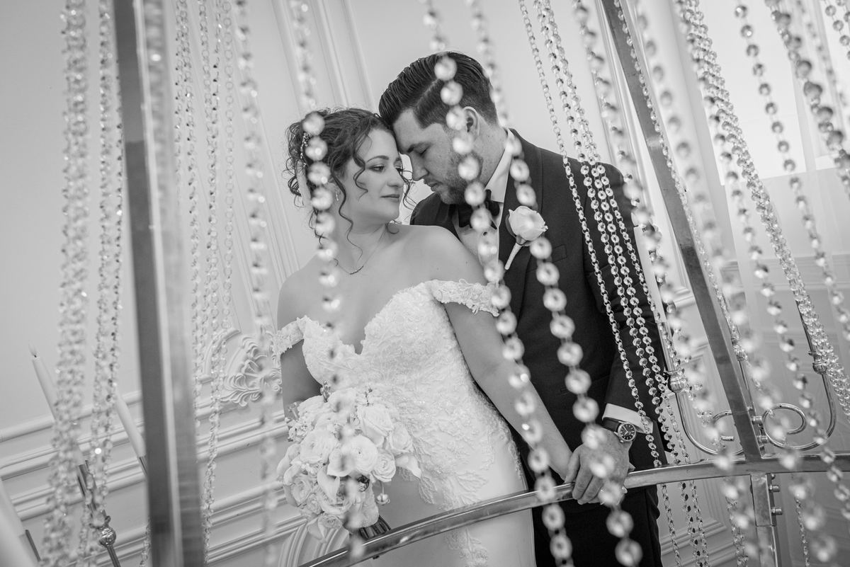 Bride and groom share an intimate moment, touching foreheads on a staircase adorned with crystal beads.