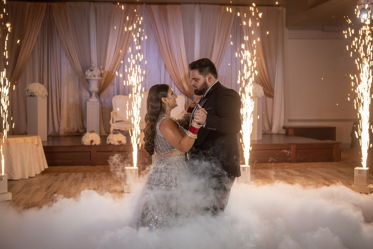 A bride and groom dance intimately on a smoky floor, surrounded by vertical sparklers casting golden light.