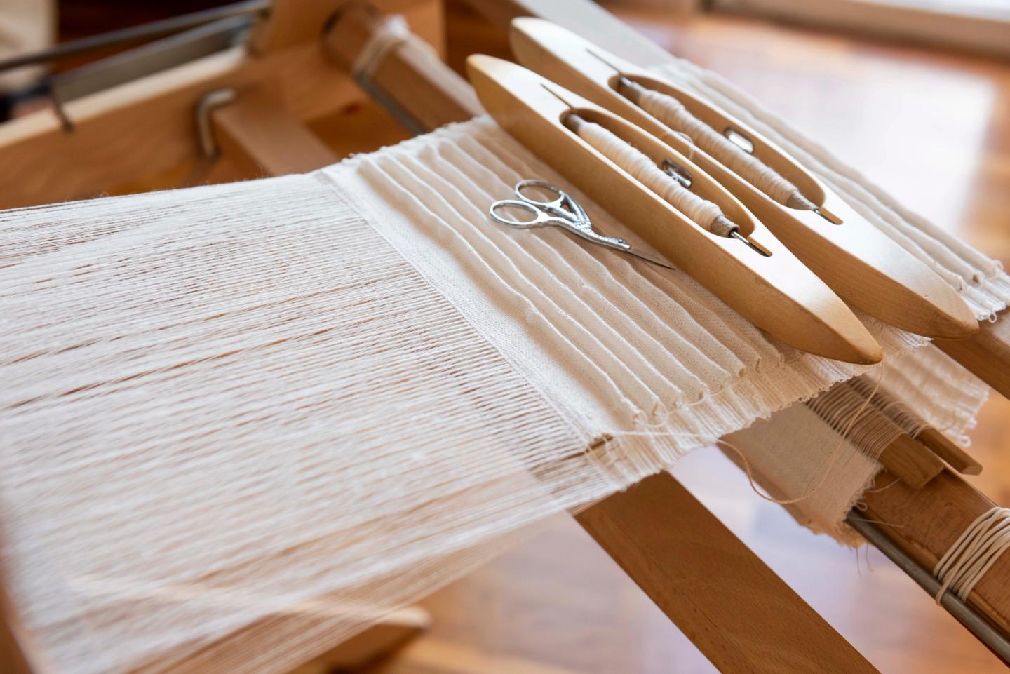 Tissage plissé blanc sur le métier, navettes et fils à l’atelier Saint Frison
