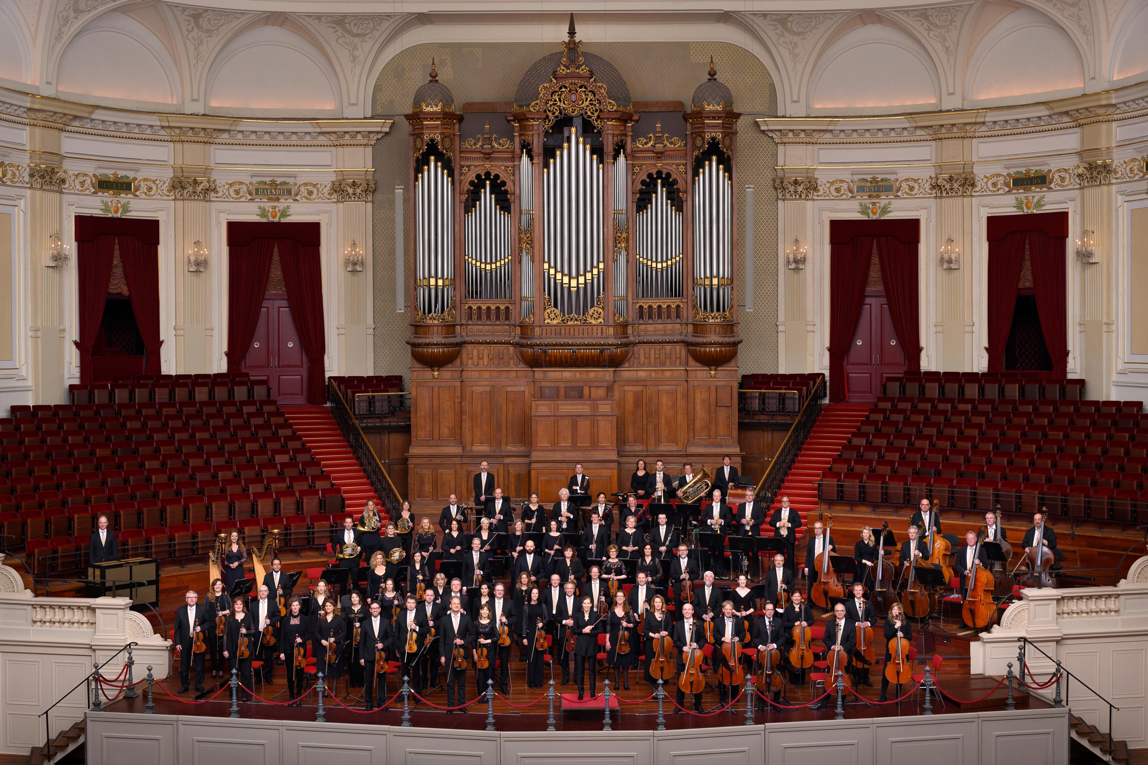 The orchestra stood on stage in front of a grand organ looking at the camera