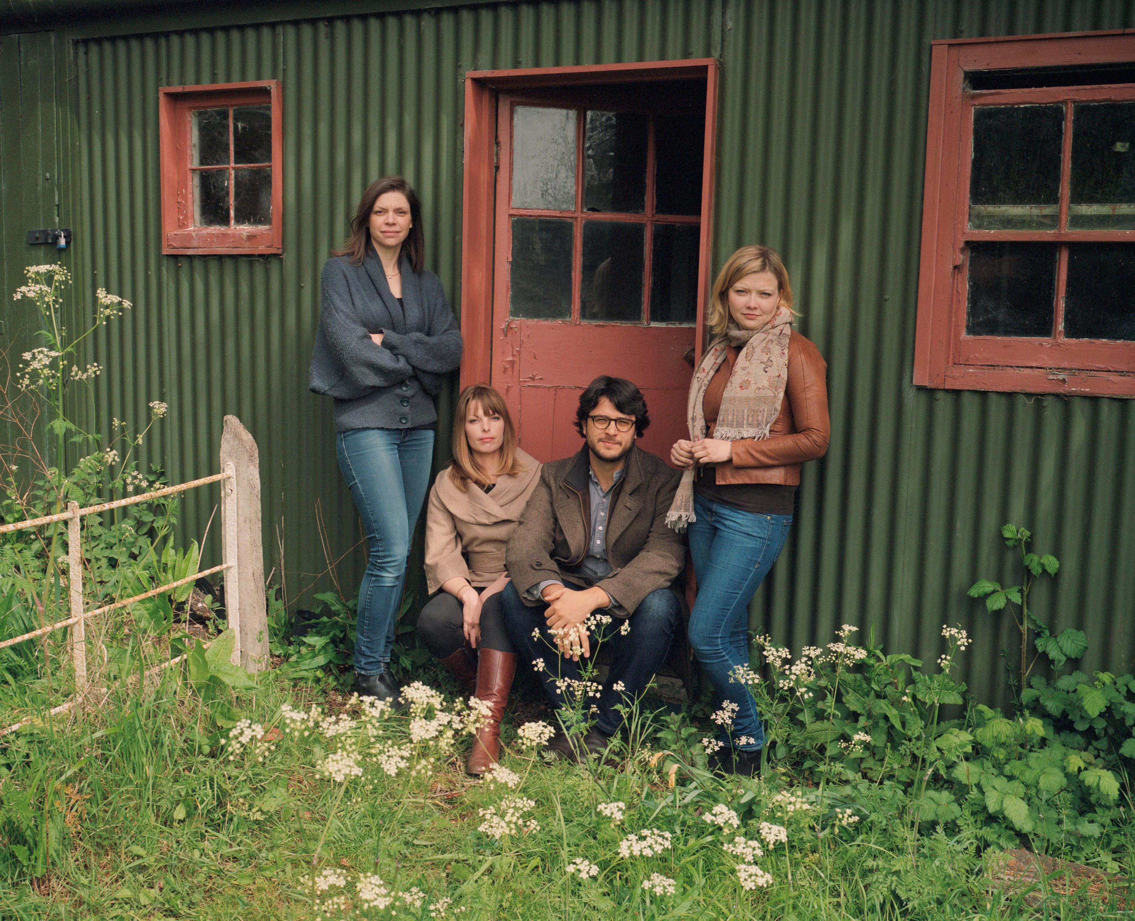 4 musicians standing outside a green corrugated iron shed in a garden