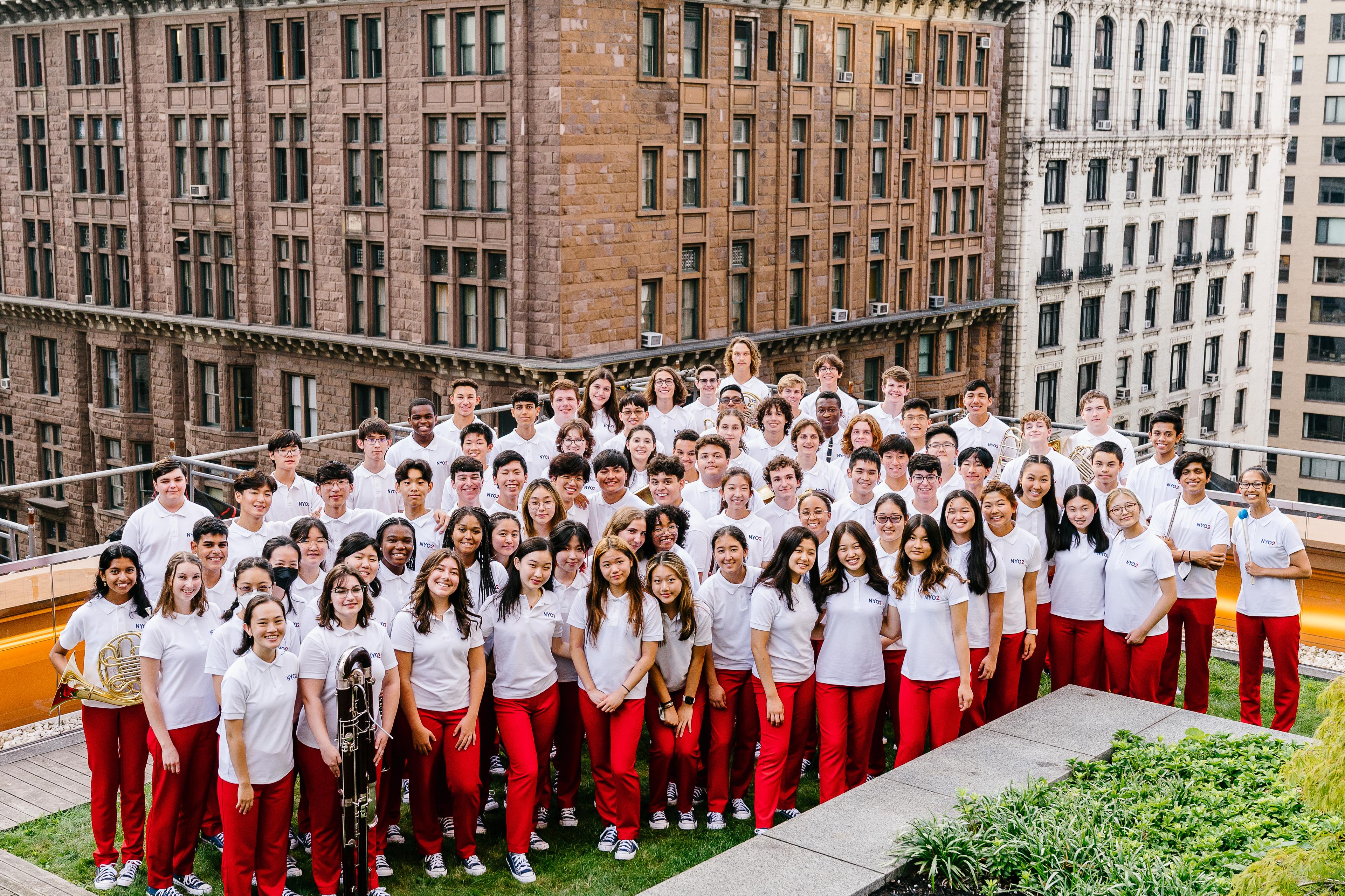 NYO2 wearing red trousers and white tops posing on a rooftop in New York and smiling at the camera