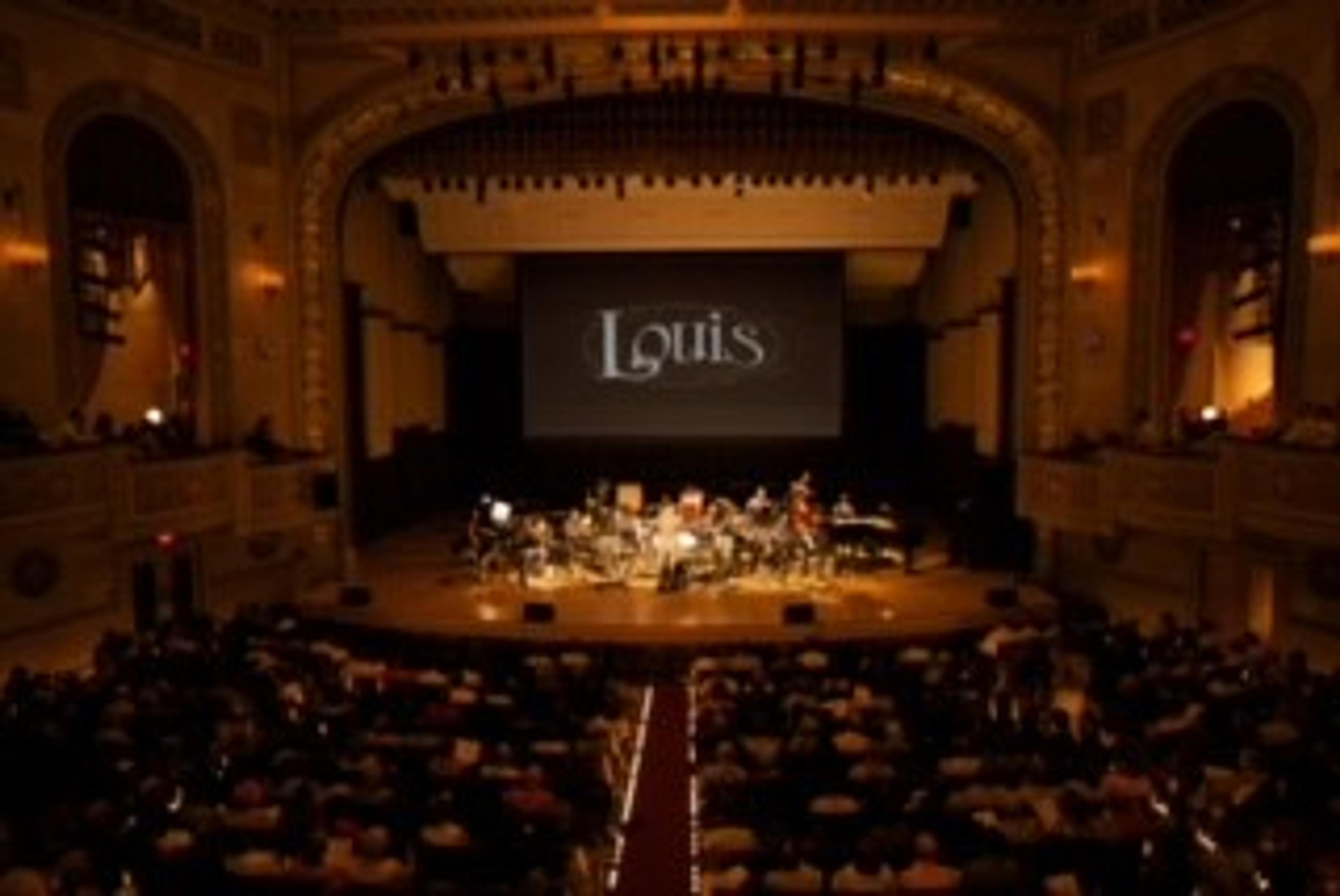 Jazz band on stage in a concert hall, with large screen behind