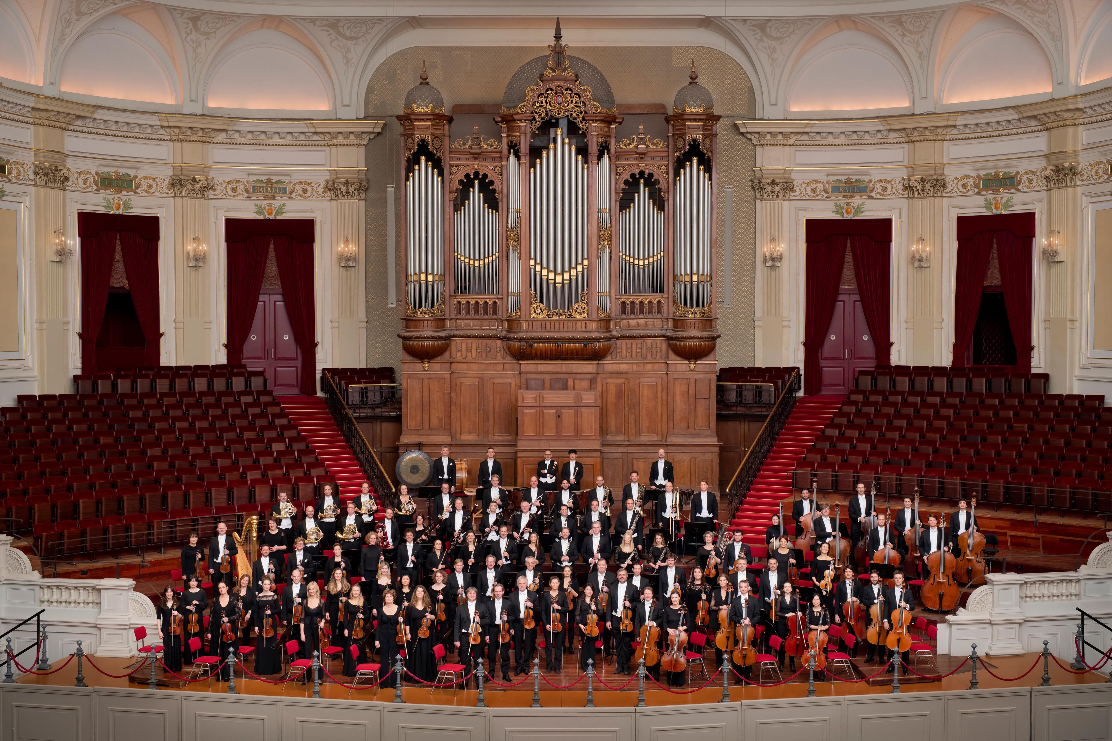 The Royal Concertgebouw Orchestra standing with their instruments on stage