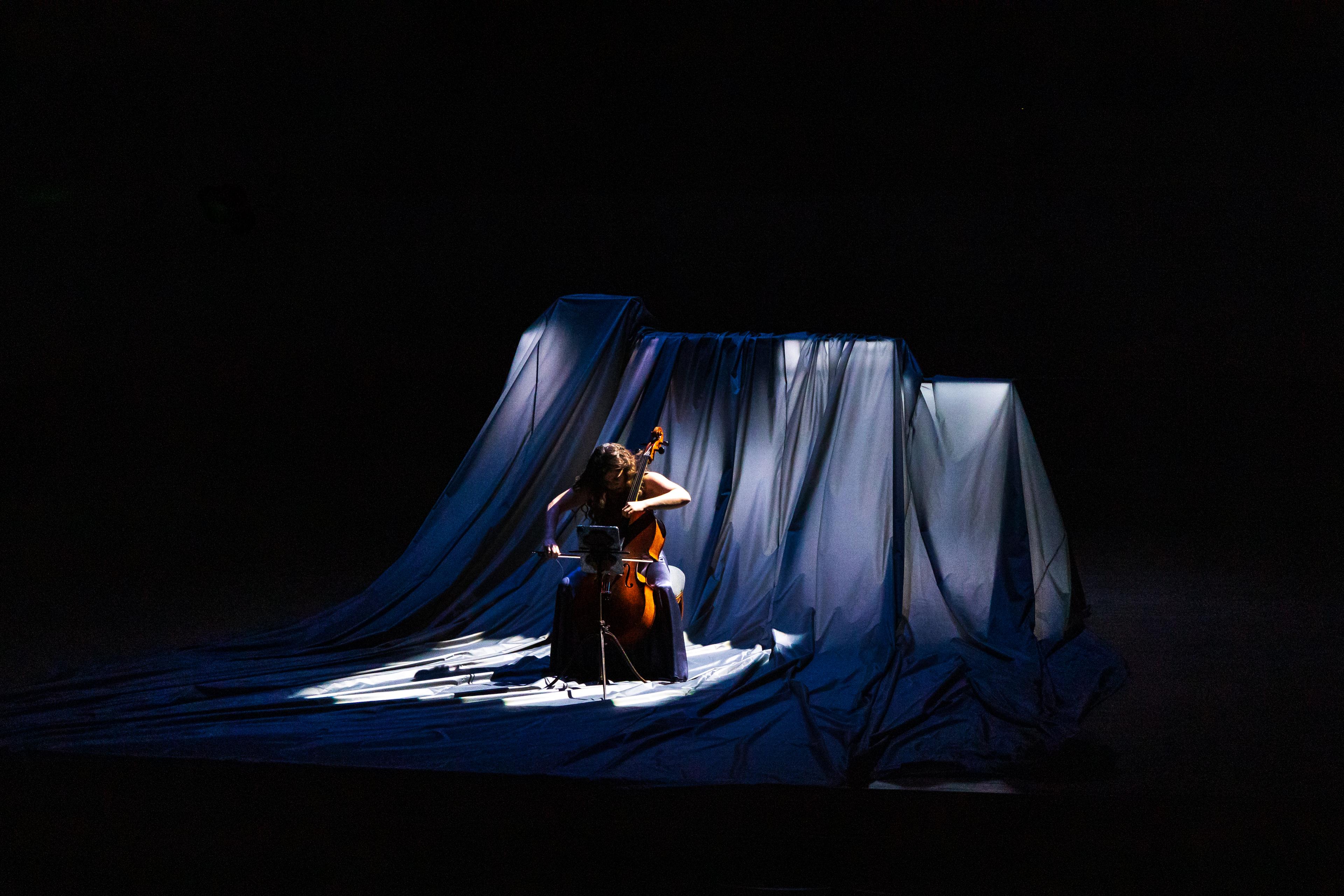 Cellist Alisa Weilerstein performing in front of illuminated dark material