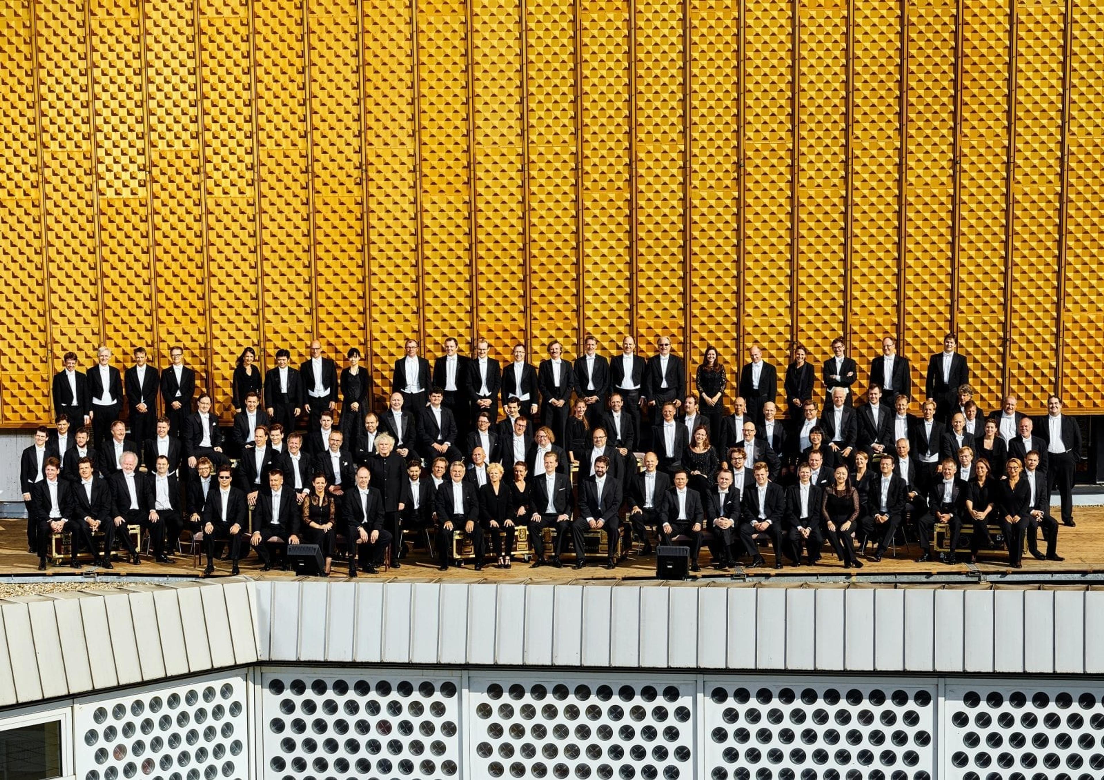 The Berliner Philharmoniker stood in formation in front of a striking yellow backdrop