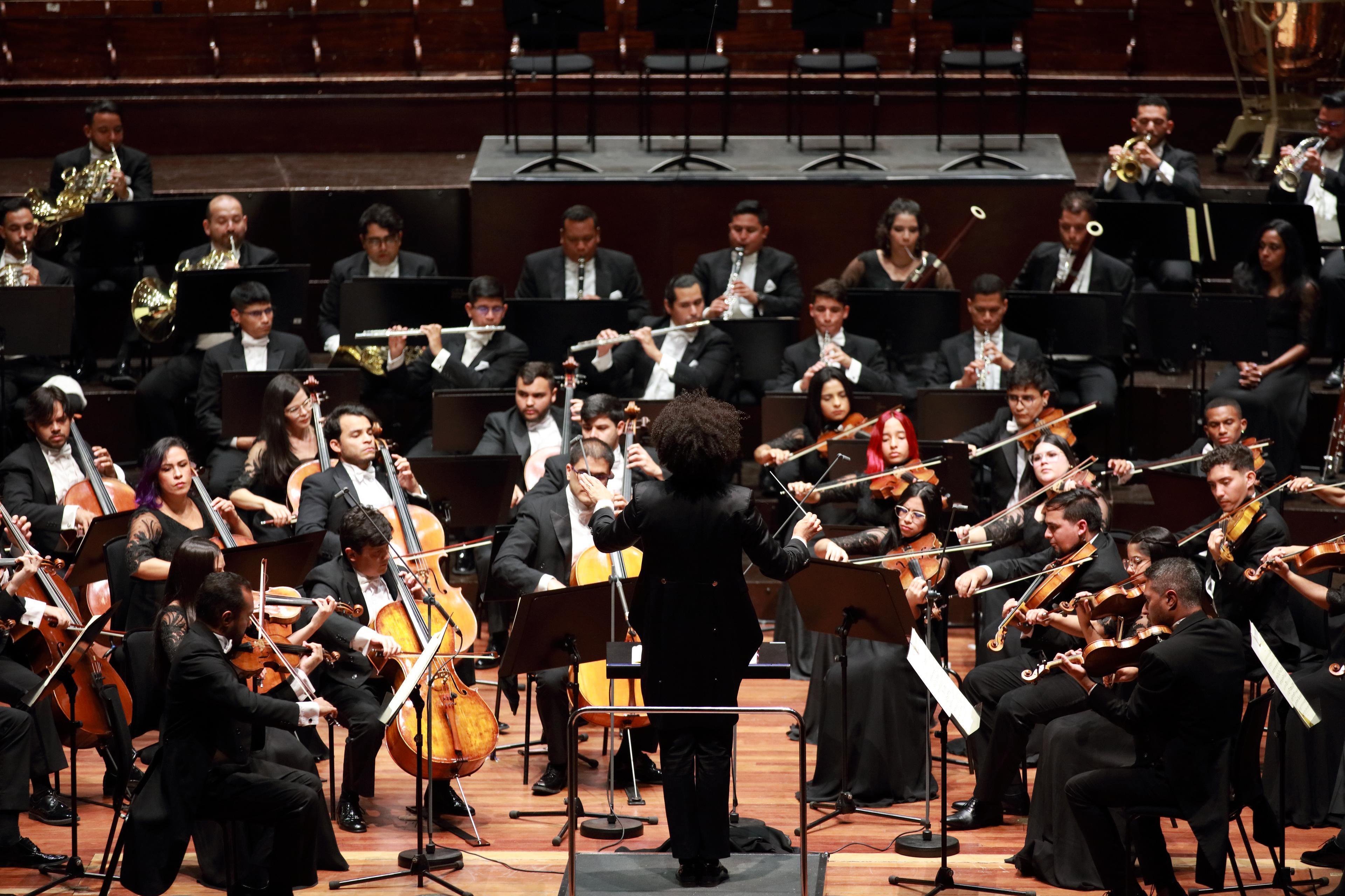 The Simón Bolívar Symphony Orchestra in formal attire playing the Edinburgh International Festival, photographed from behind the conductor