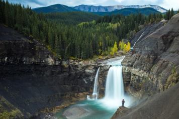 Zoomed out wide shot of a hiker looking at a beautiful waterfall plunging onto sandstone rock below