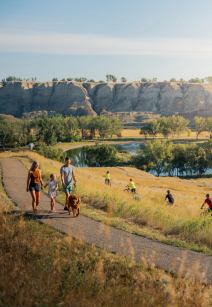 Family walking with a dog while others are mountain biking in Echo Dale Park in Medicine Hat.