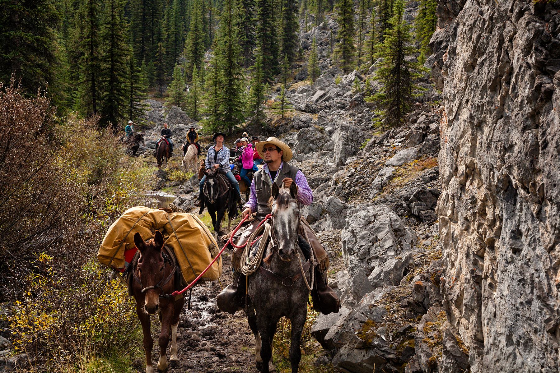 A tour group on horseback riding through a rocky canyon in Banff National Park.