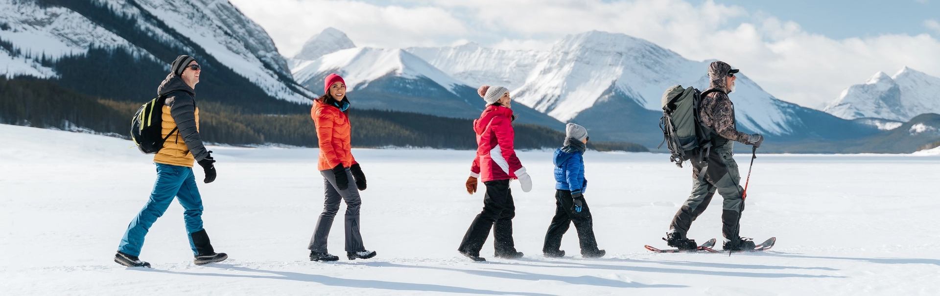 A family walk behind guide on snowshoes over a frozen lake in Canmore
