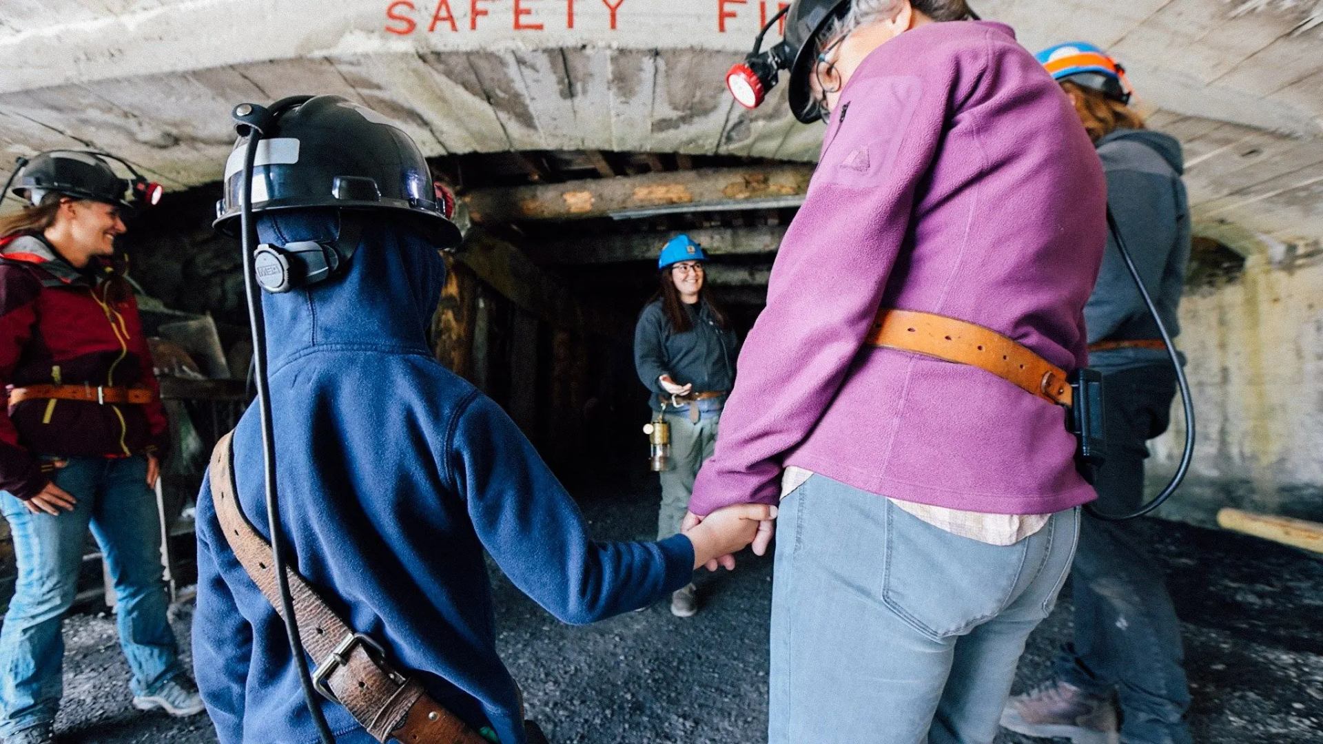 Mother holding child's hand wearing helmet lights at the Bellevue Underground Mine.