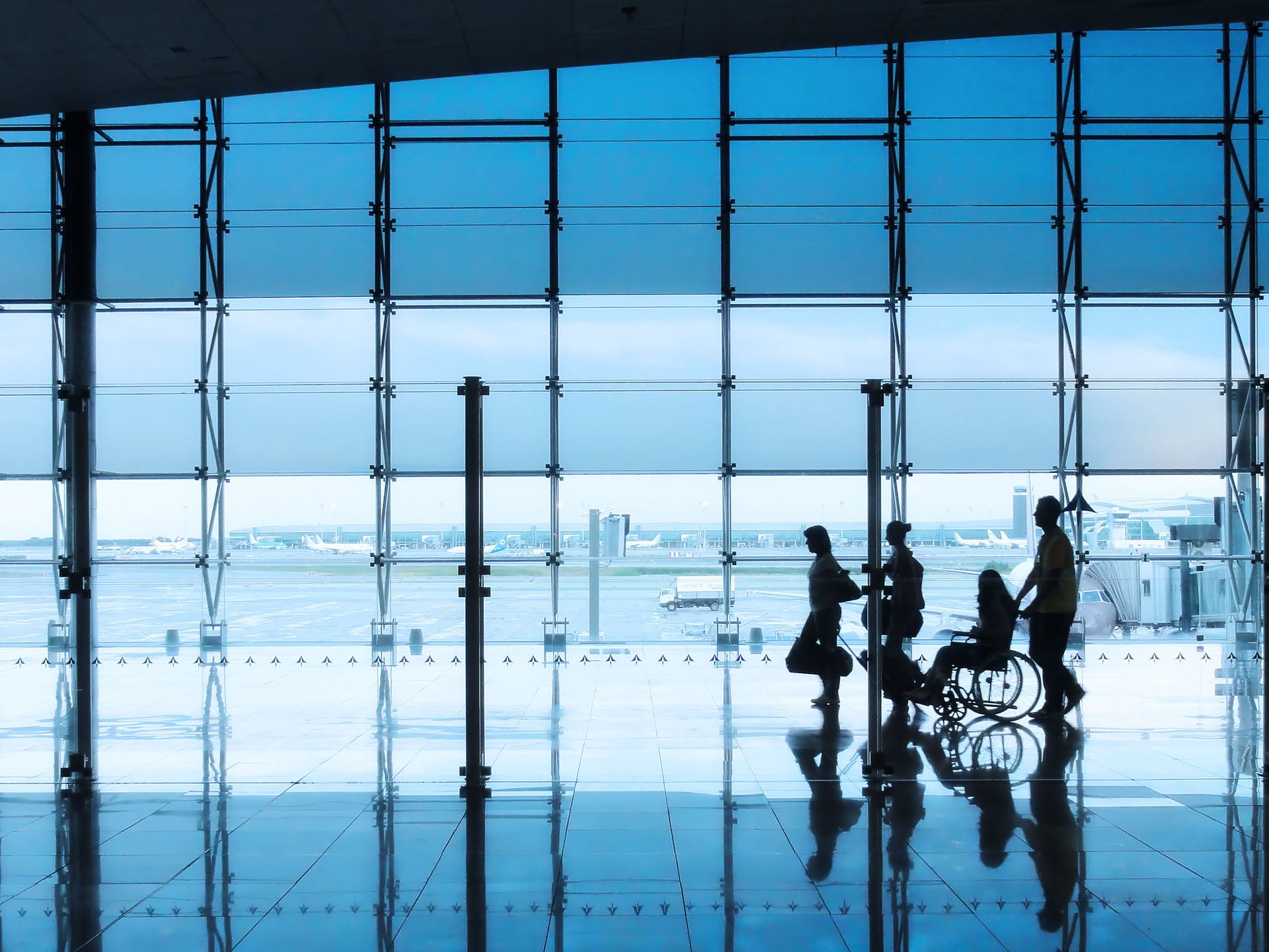 A silhouette of a group moving through an airport, including a person in a wheelchair.